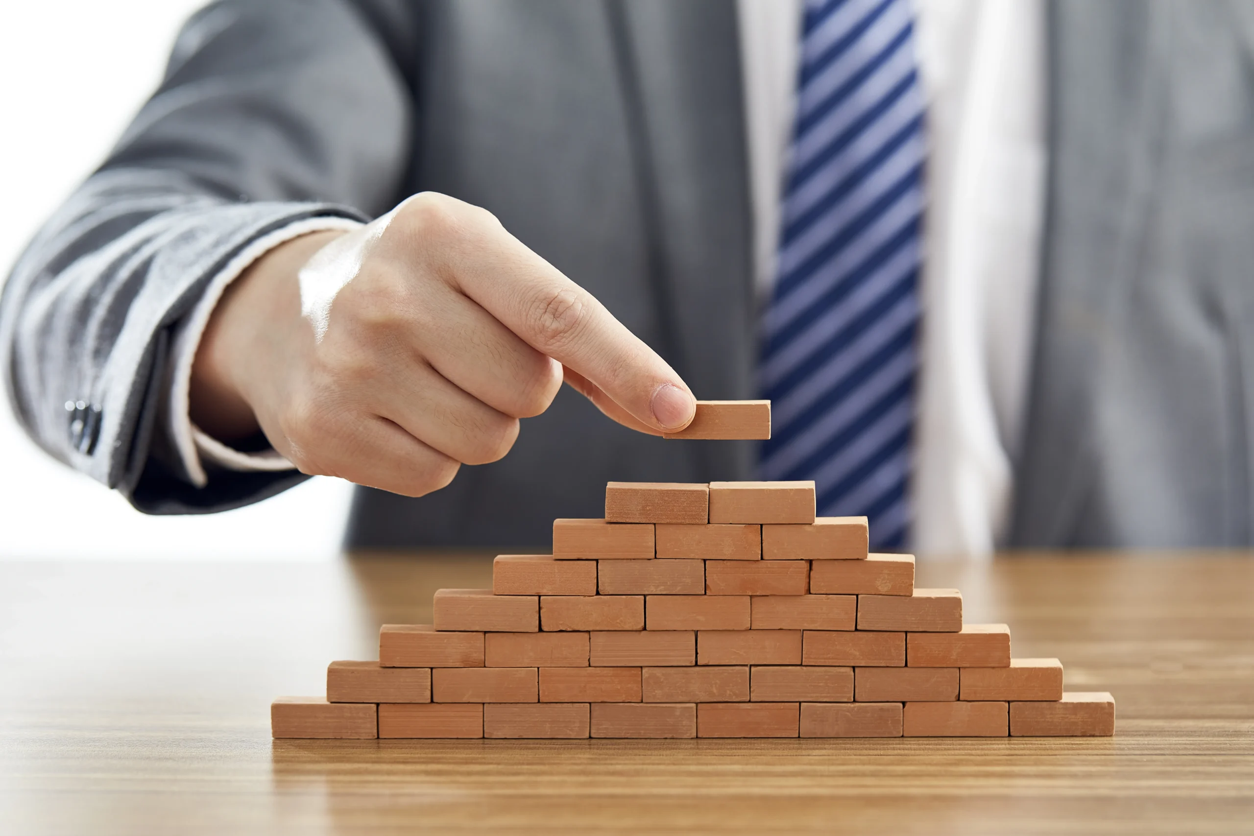 businessman suit putting last piece pyramid using wooden blocks scaled 2 - Pilot India